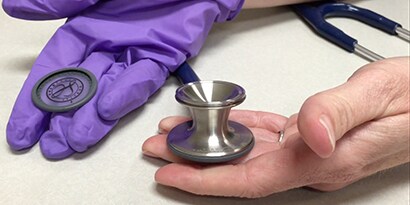 Mains tenant la tête de stéthoscope 3M™ Littmann® ClassicIII™.
